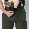 Close-up of a man wearing dark green drawstring pants branded with FN Firearms, showing a pistol and spare magazine holstered inside the waistband with a tactical belt system