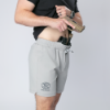 A man wearing light gray FN-branded drawstring shorts demonstrates concealed carry by drawing a pistol afrom a black tactical holster belt